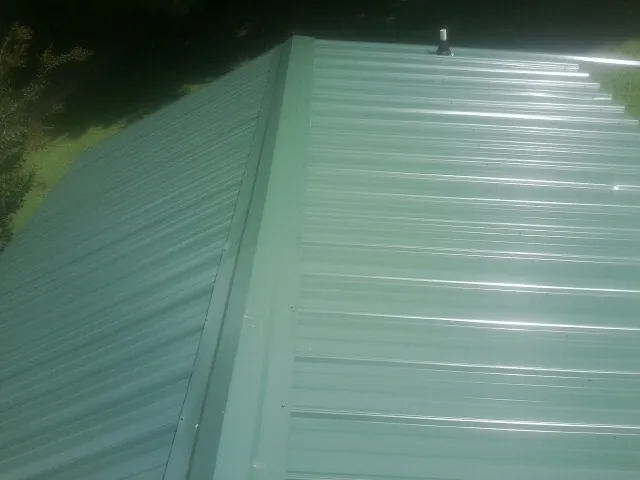 New green metal panels meeting at the ridge of a roof — Flat Roof Repair work by our crew in Cedar Hill