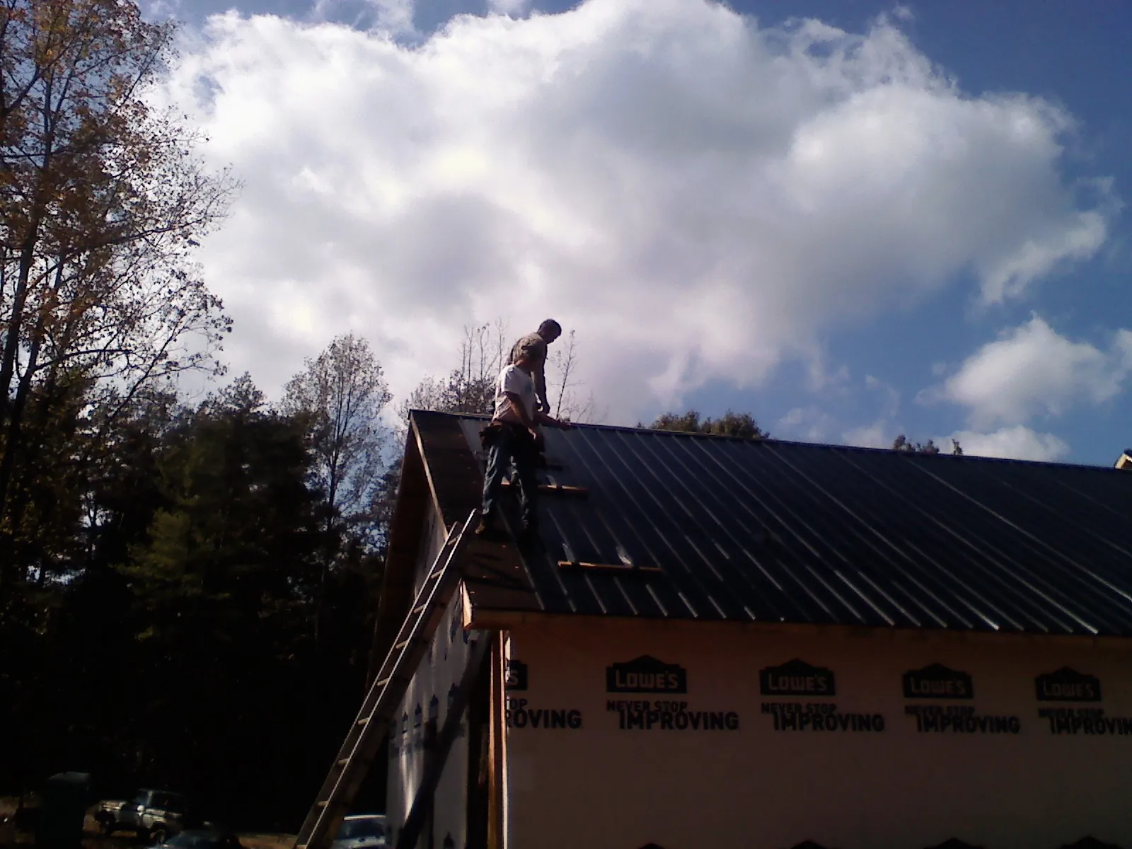 Roofer fastening dark metal panels high against a cloudy sky, from a Roof Inspection job in Cedar Hill